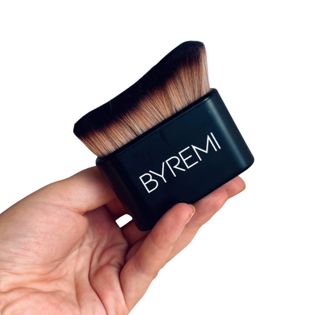 Makeup brush with black handle and 'BYREMI' branding held in a hand against a white background tanning brush