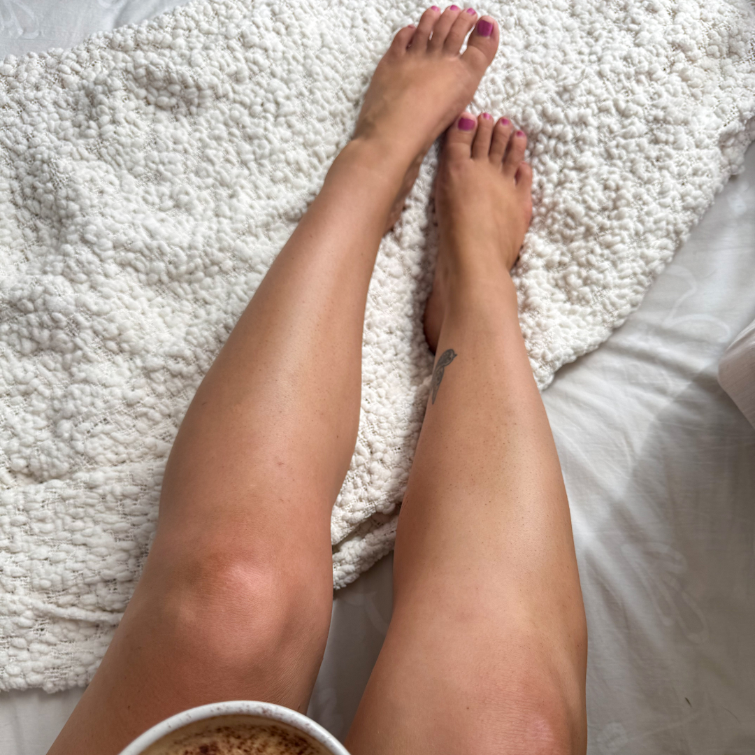 Close-up of tanned legs on a textured white surface with a cup held in one hand.
