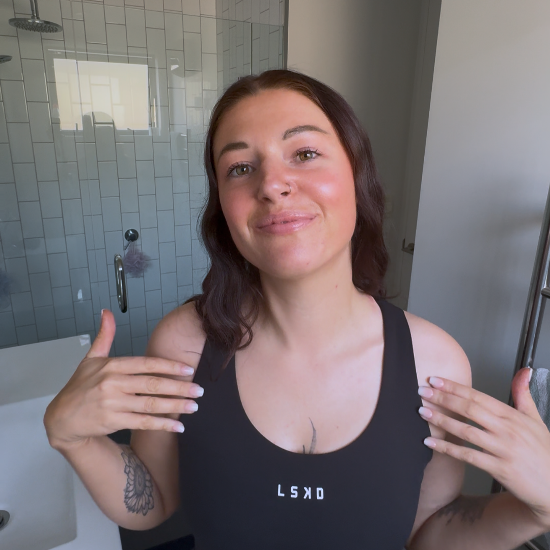 Woman in a black tank top standing in a bathroom showing self tan